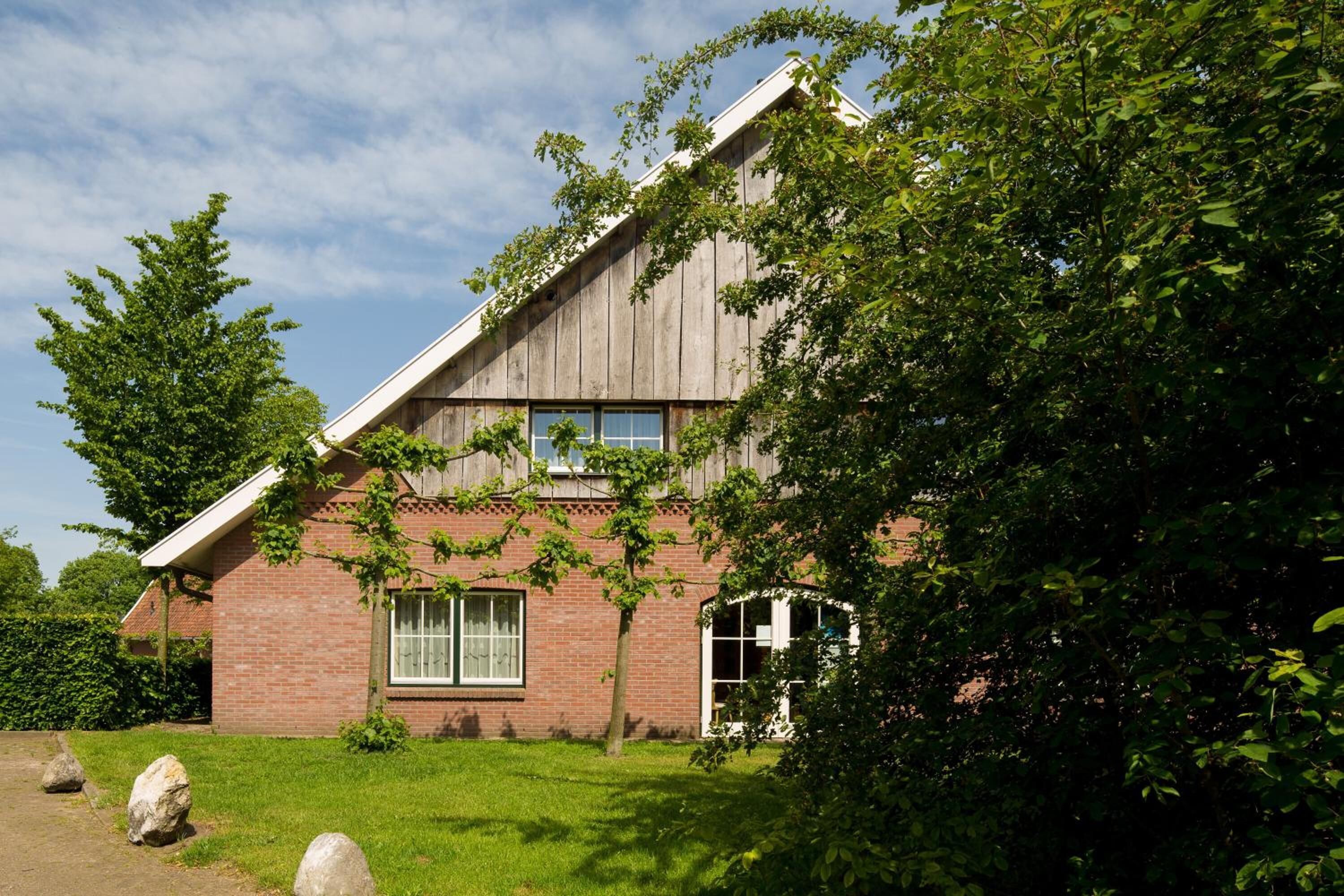 Een bakstenen huis met een schuin dak, grote ramen en een verzorgd gazon.