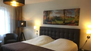A hotel room with a large bed, two bedside lamps, a chair, a desk, and a painting on the wall.