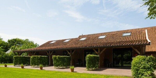 Un bâtiment doté d’un toit en tuiles, de grandes fenêtres et d’un espace extérieur couvert aménagé avec des sièges.
