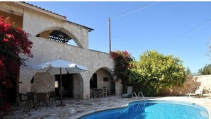 Un edificio de piedra con piscina, mobiliario exterior y abundante vegetación.