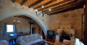 Ein rustikales Wohnzimmer mit Steinwand, Holzbalken, einer Couch, einem Fernseher und einem Kamin.