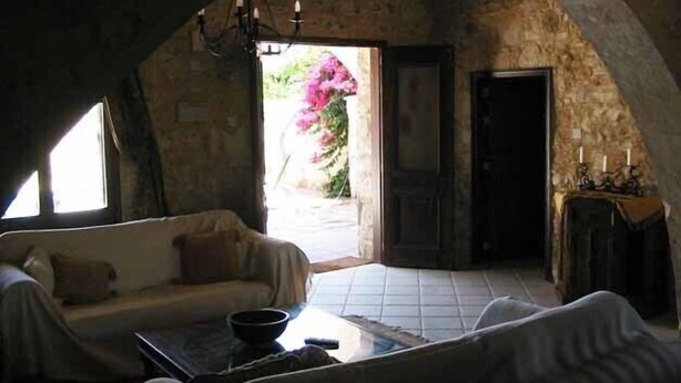 Una habitación rústica con pared de piedra, techo de madera, un sofá, una mesa y una puerta que da al exterior.