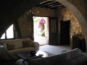 Una habitación rústica con pared de piedra, techo de madera, un sofá, una mesa y una puerta que da al exterior.