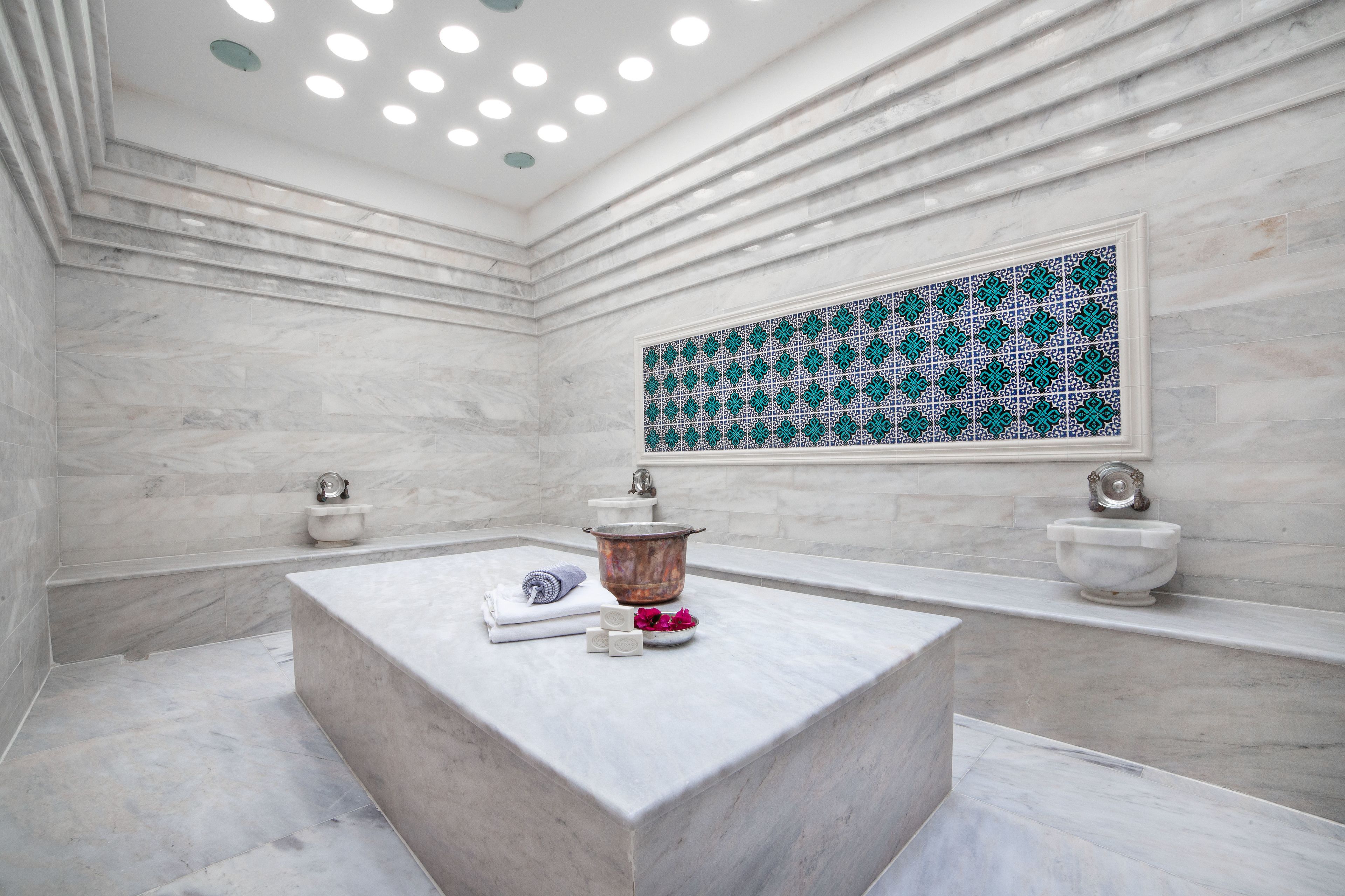A modern bathroom with a marble vanity, a large decorative tile wall, and a built-in bathtub.