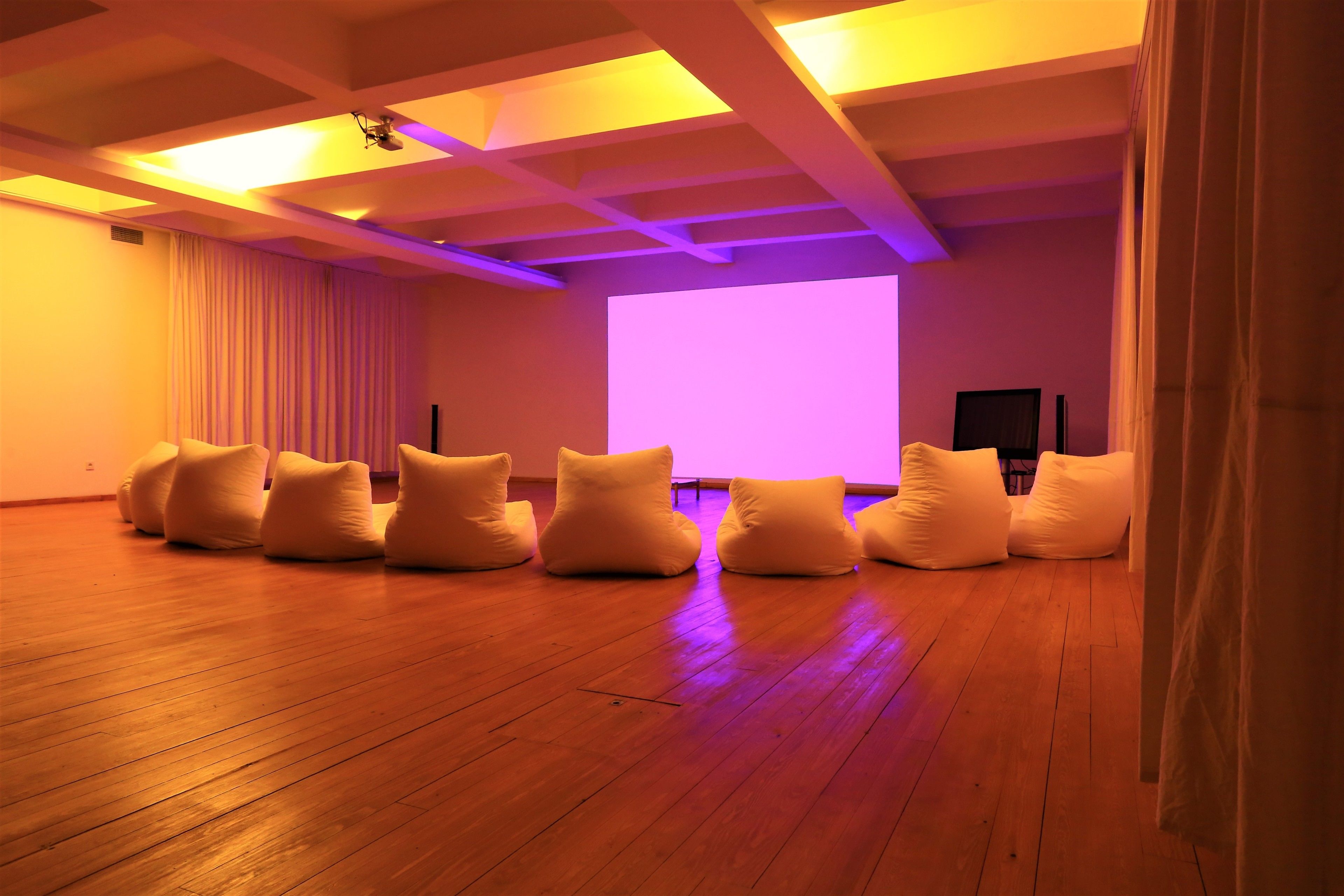 A spacious room with wooden flooring, a large screen, and several white bean bag chairs arranged in a row.