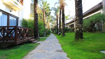 A stone pathway flanked by palm trees and greenery, leading to a building with balconies.