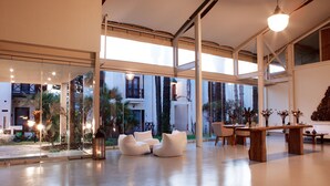 A modern interior with large glass windows, white furniture, and a dining area with a wooden table and chairs. - The LifeCo Bodrum Well - Being Center - Adults Only (Bodrum)