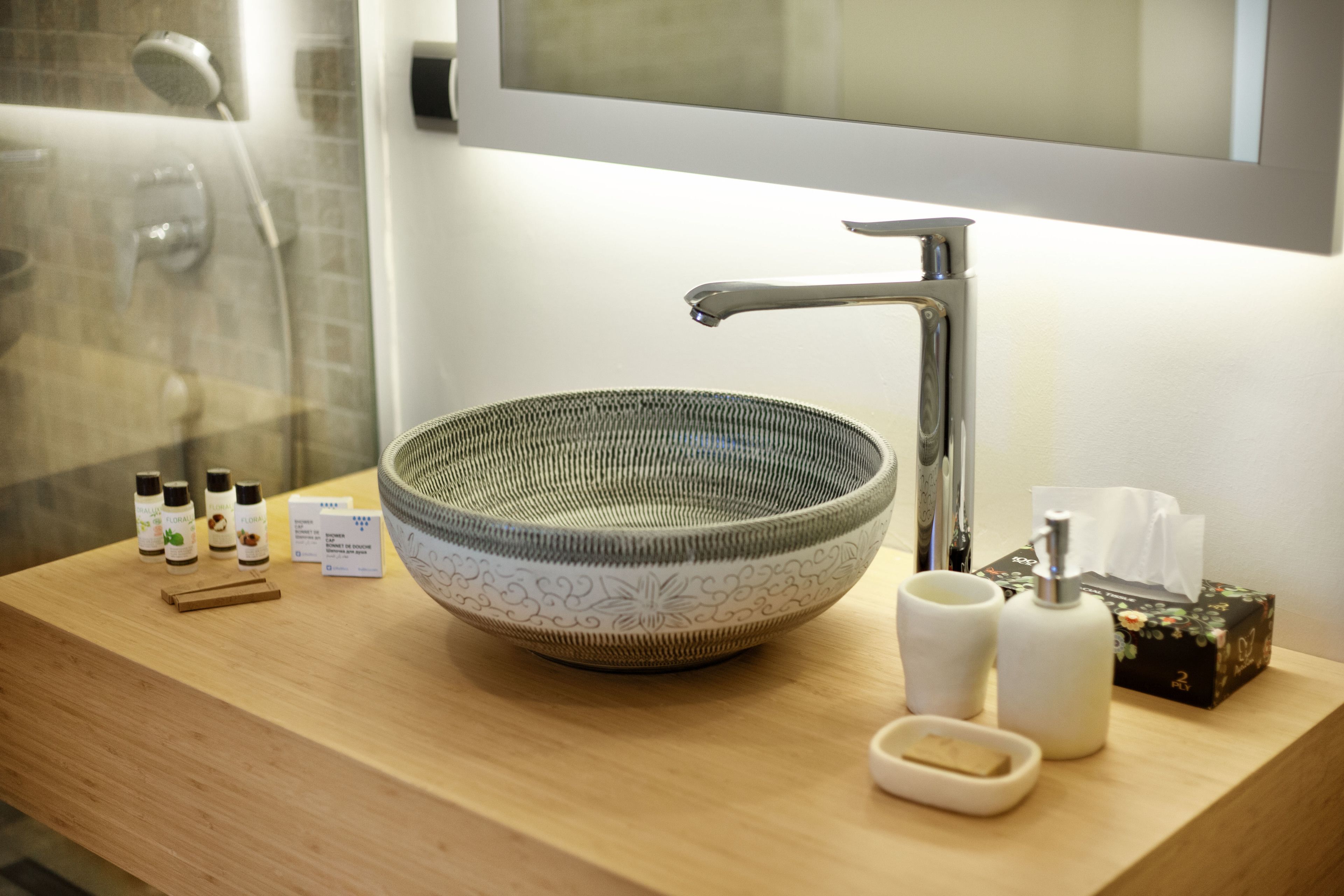 A bathroom with a wooden vanity, a large decorative bowl sink, a mirror, and toiletries.