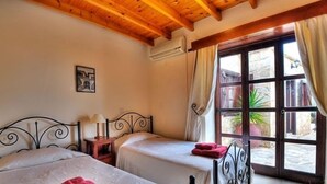 Une chambre avec deux lits, une fenêtre avec des rideaux, une petite table avec une lampe et un climatiseur fixé au mur.