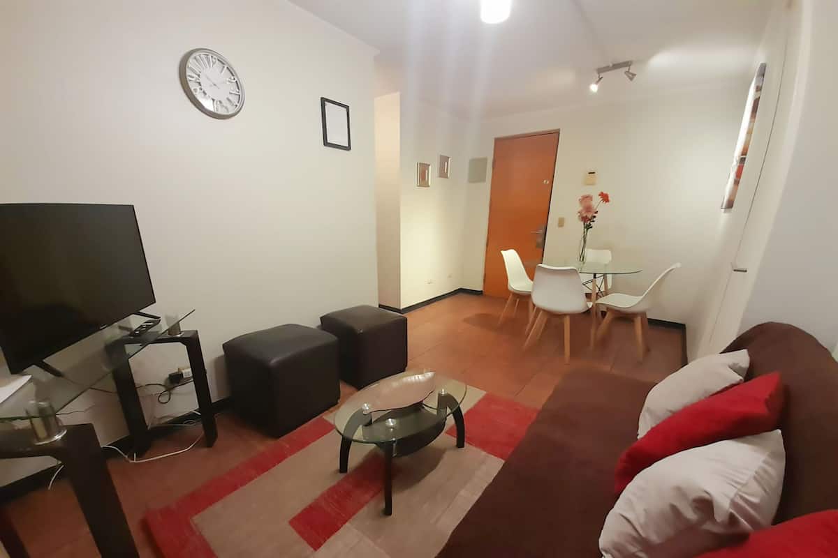 A living room with a TV, sofa, ottomans, and a dining area with chairs and a table.
