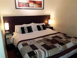 A neatly made bed with a patterned bedspread, two bedside lamps, and a framed picture above the bed. - VIP Apartments Chile (Santiago)