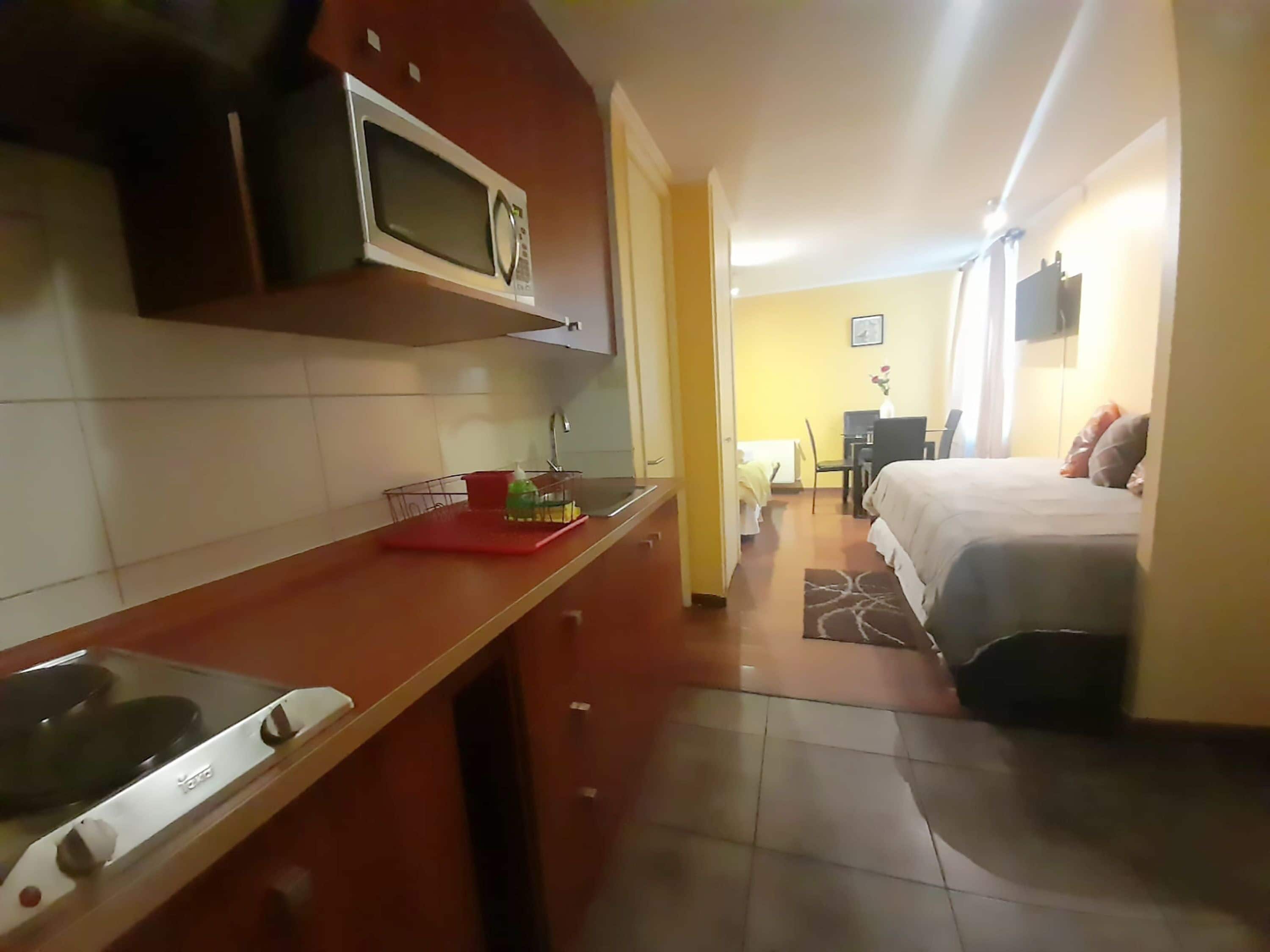 Une chambre d’hôtel de taille réduite, équipée d’une kitchenette, d’un lit, d’un petit bureau et d’une chaise.