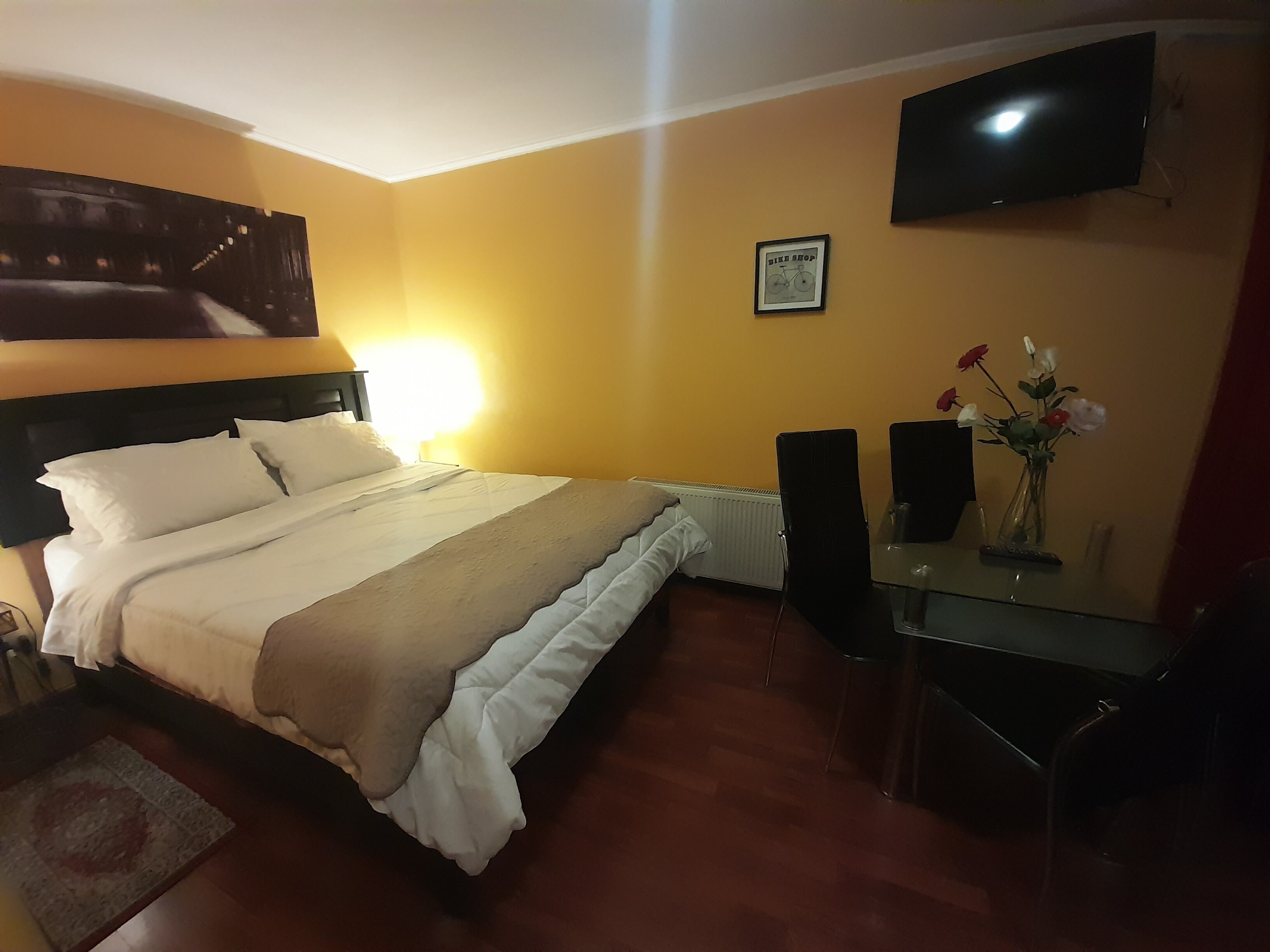 A hotel room with a bed, a desk with a chair, a TV, and a framed picture on the wall.