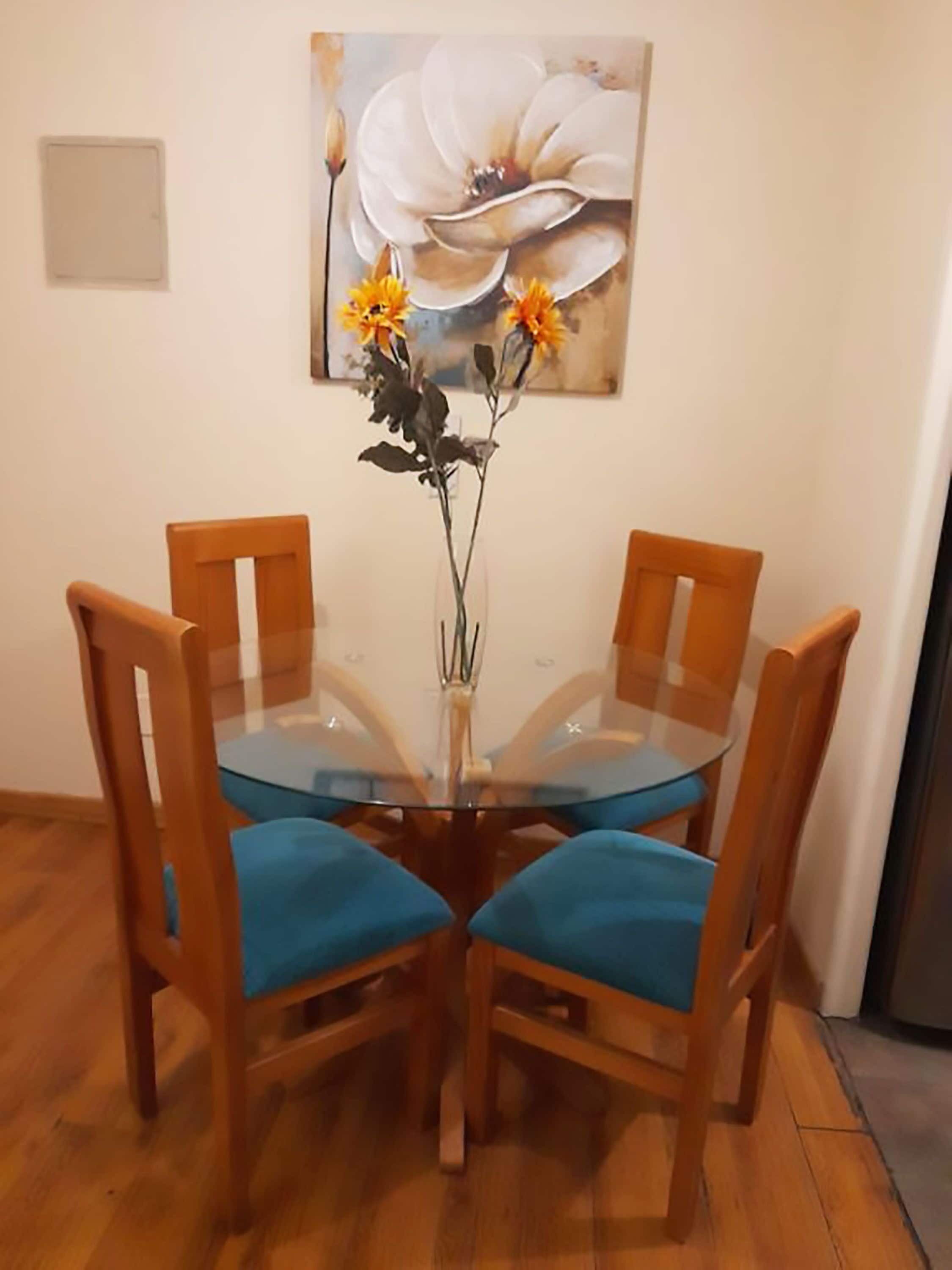 Un coin repas avec une table en verre entourée de chaises en bois dotées de coussins bleus. Un vase rempli de fleurs est posé sur la table.