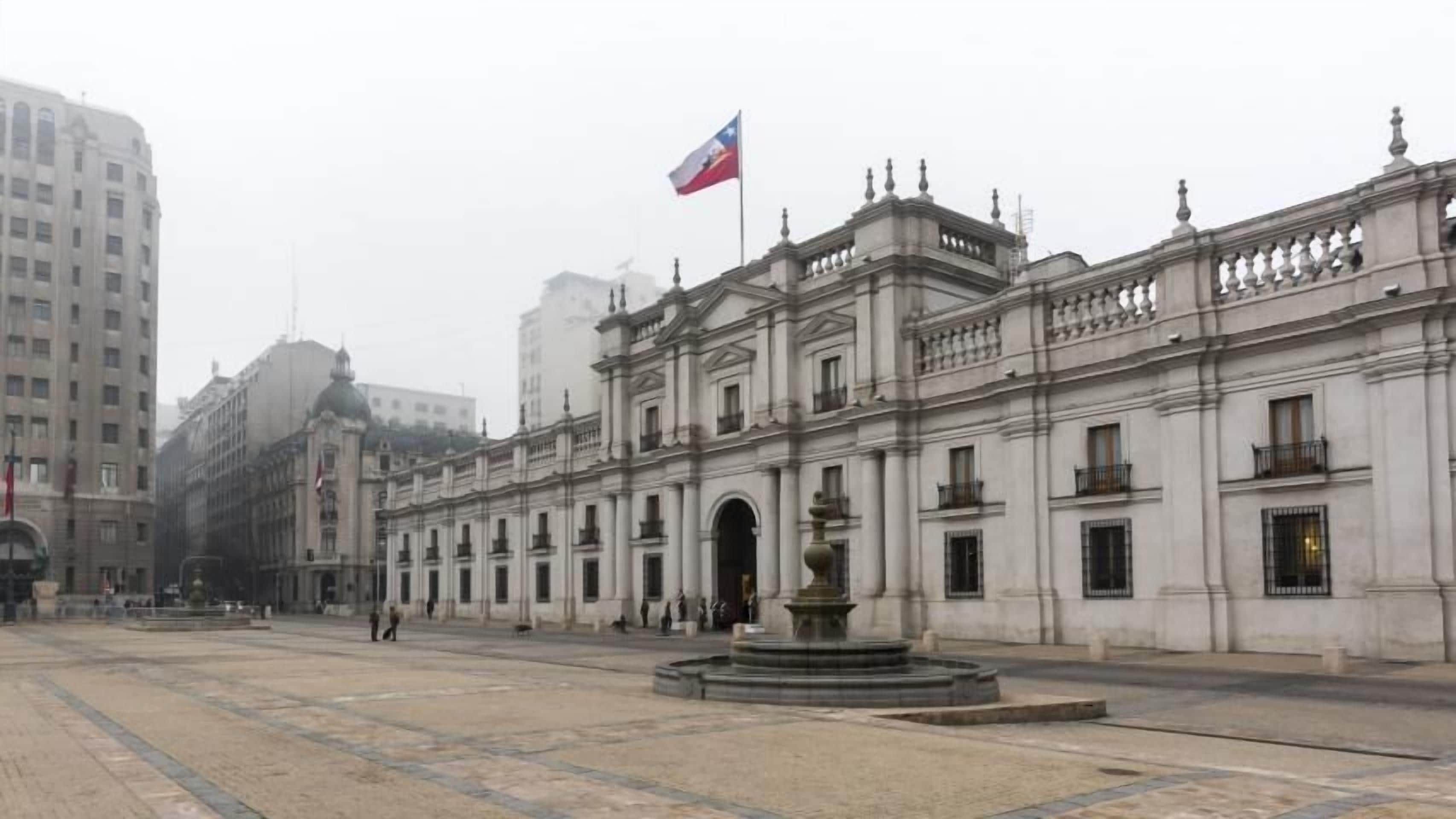 Un grand bâtiment historique, orné d’un drapeau bien visible, doté d’une fontaine centrale et entouré d’une vaste place.