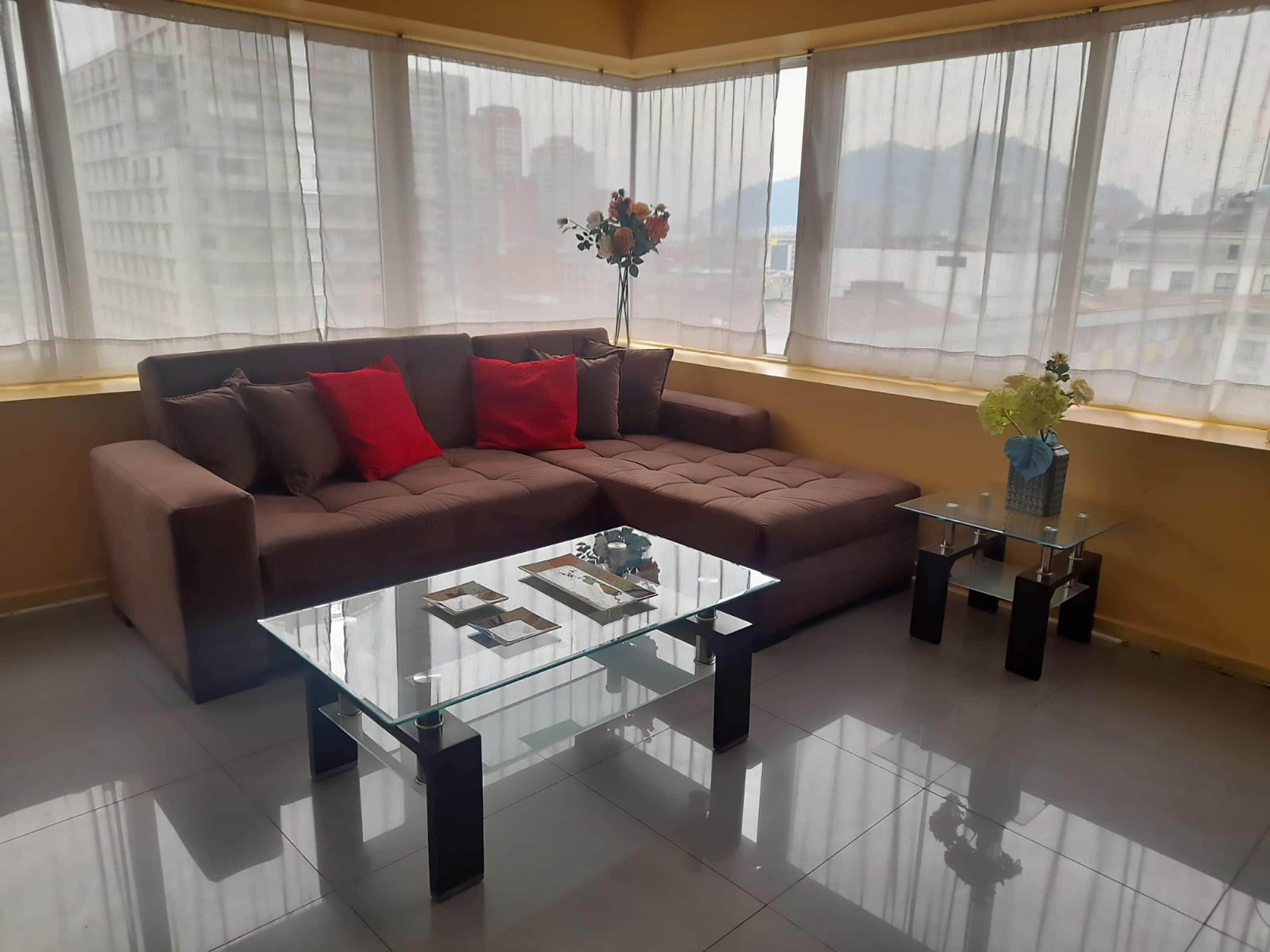 A modern living room with a brown sectional sofa, a glass coffee table, and a vase with flowers on a small table.