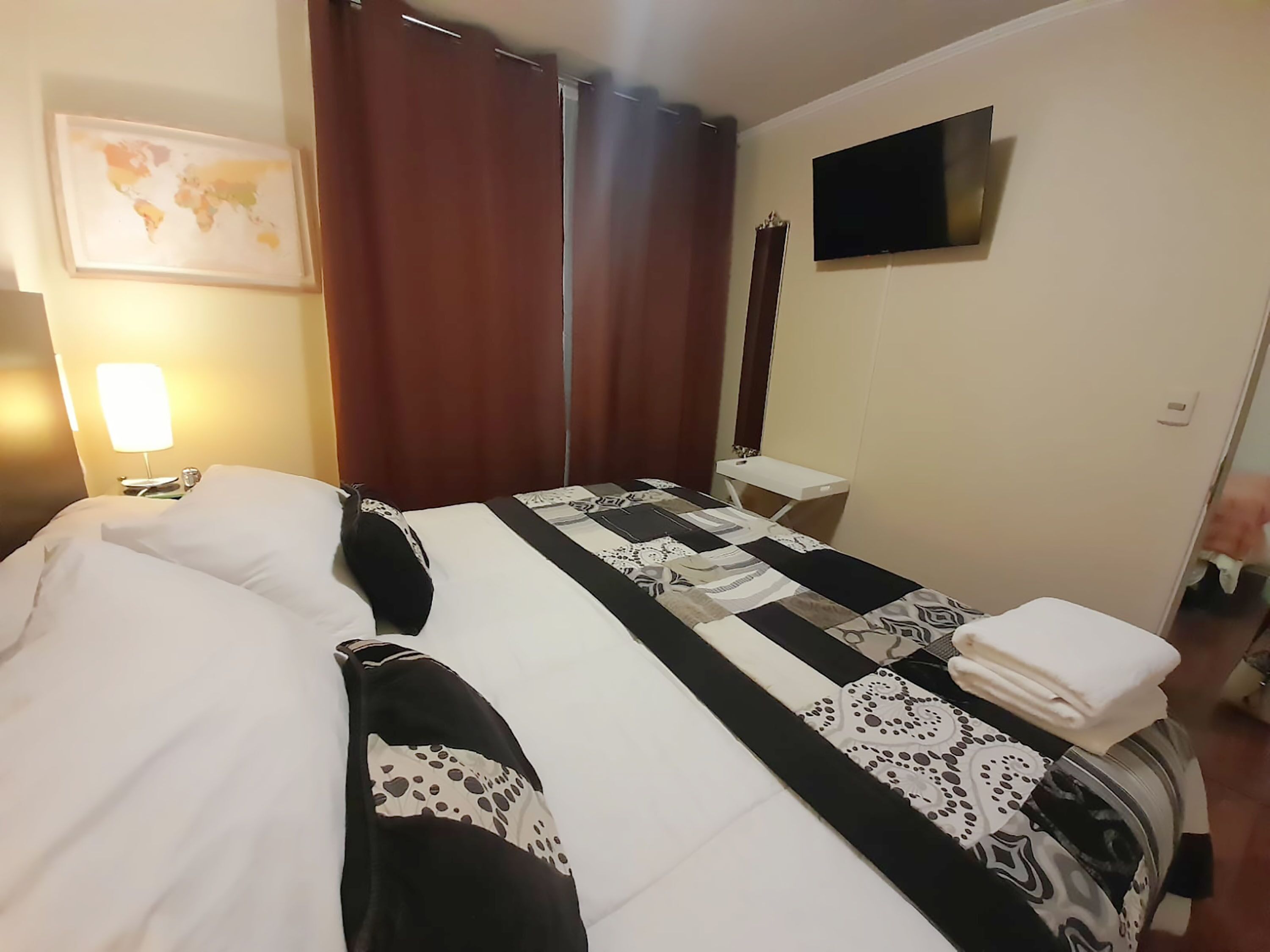 Quarto de hotel com cama, escrivaninha, televisão e mapa na parede.