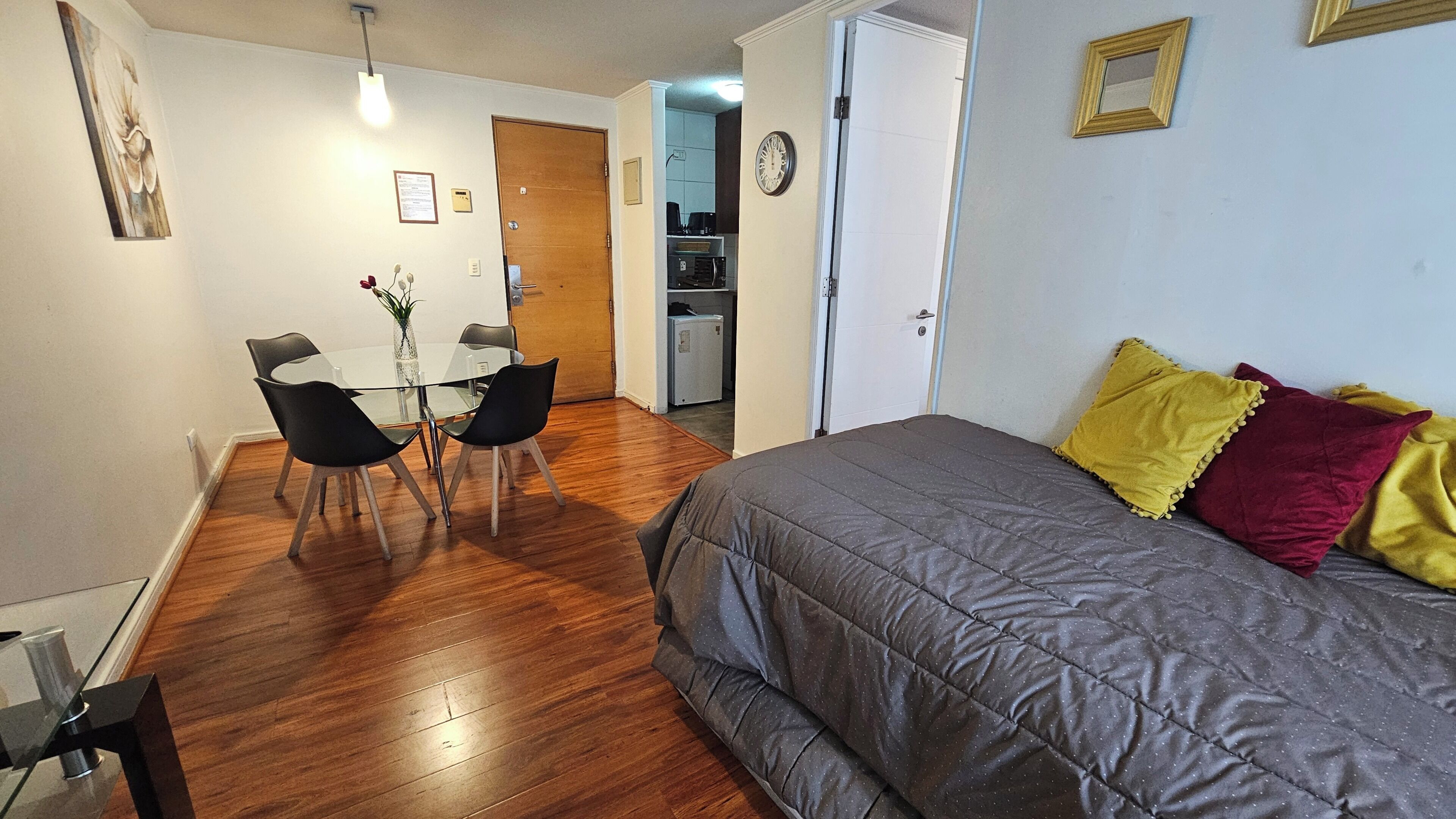 Un dormitorio con cama, una mesa de comedor con sillas, una kitchenette y una puerta que da a otra habitación.