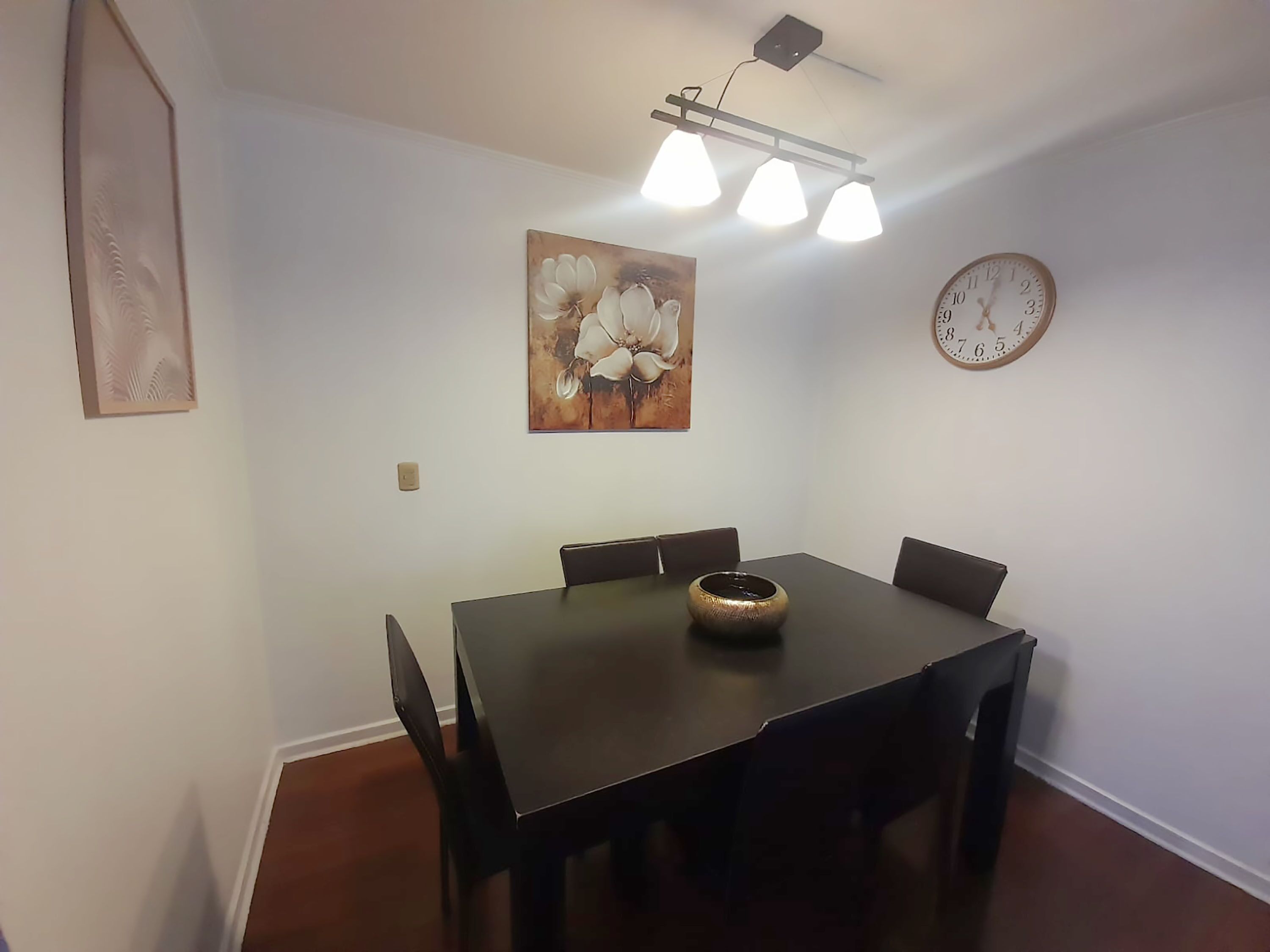 Un'area pranzo con un tavolo, sedie, un orologio e un quadro floreale appeso al muro.