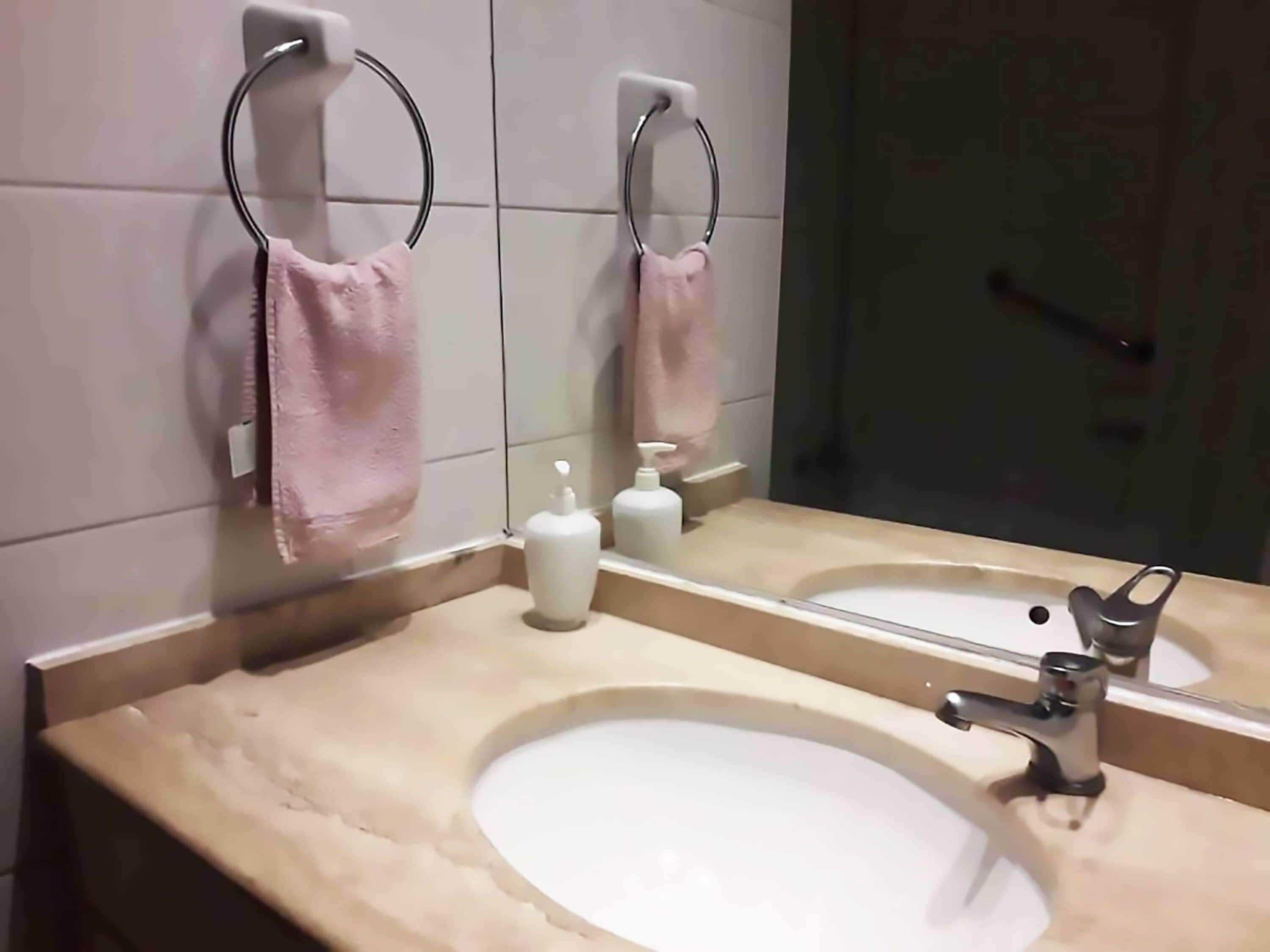 Une salle de bain avec un lavabo beige, un miroir et deux porte-serviettes ornés de serviettes roses.