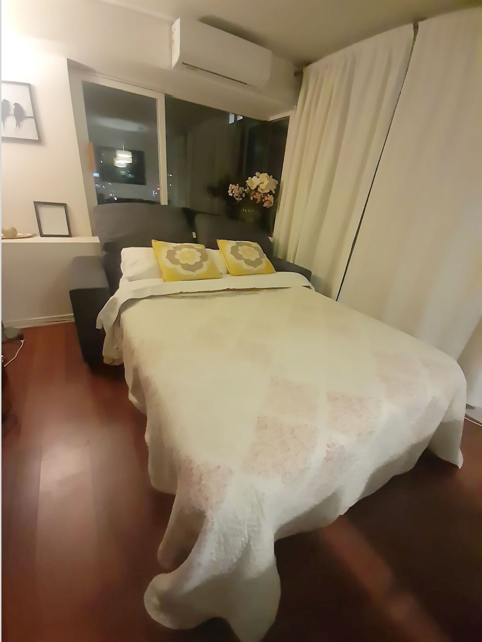 Un dormitorio con una cama, una ventana, una mesita de noche y un aire acondicionado instalado en la pared.