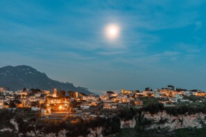 A coastal town at dusk with illuminated buildings and a prominent mountain in the background.