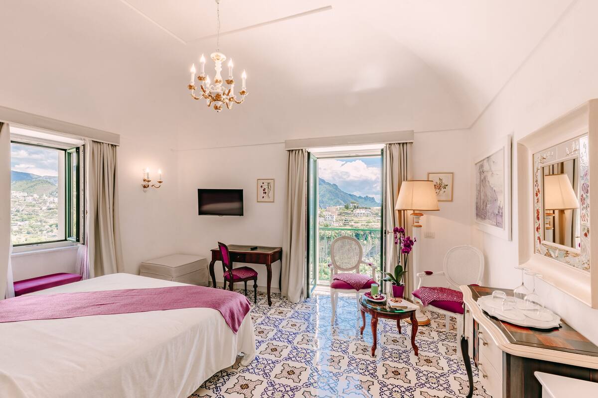Une chambre d’hôtel avec un lit, un bureau, une chaise, une table avec une lampe et une vue sur les montagnes.