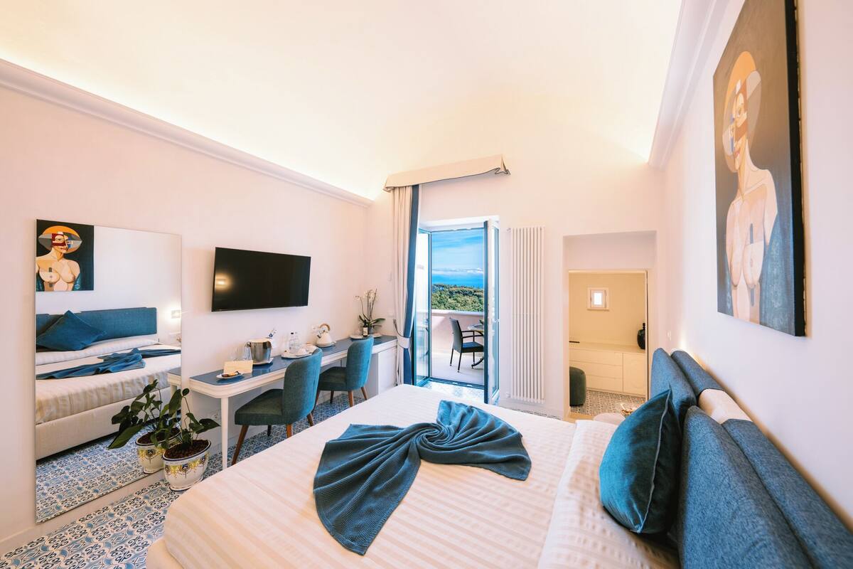 Une chambre d’hôtel avec un lit, un bureau, une chaise, une télévision et un balcon avec vue.
