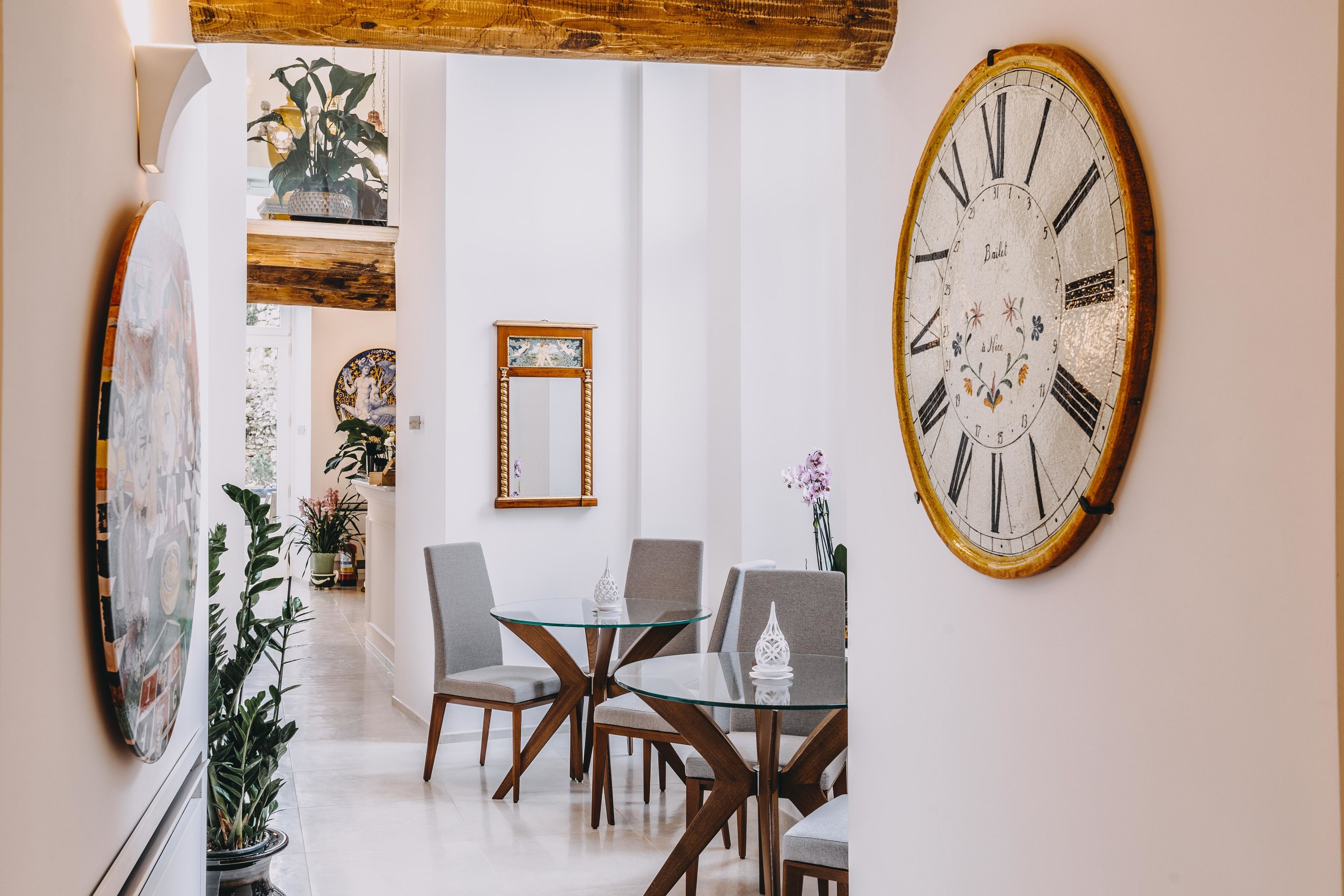 Uma sala de jantar com uma mesa de vidro e cadeiras de madeira, um relógio de parede grande e obras de arte emolduradas.