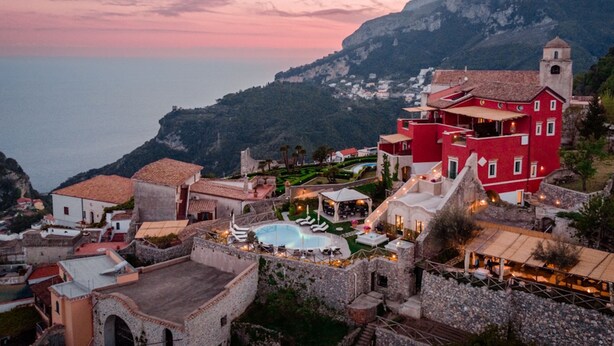 A coastal village with a prominent red building, a swimming pool, and terraced gardens. - Palazzo Pascal - Amalfi Coast Luxury Experience (Scala)
