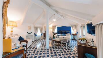 A hotel room with a high ceiling, a bed with a blue headboard, a dining area with a table and chairs, and a patterned floor.