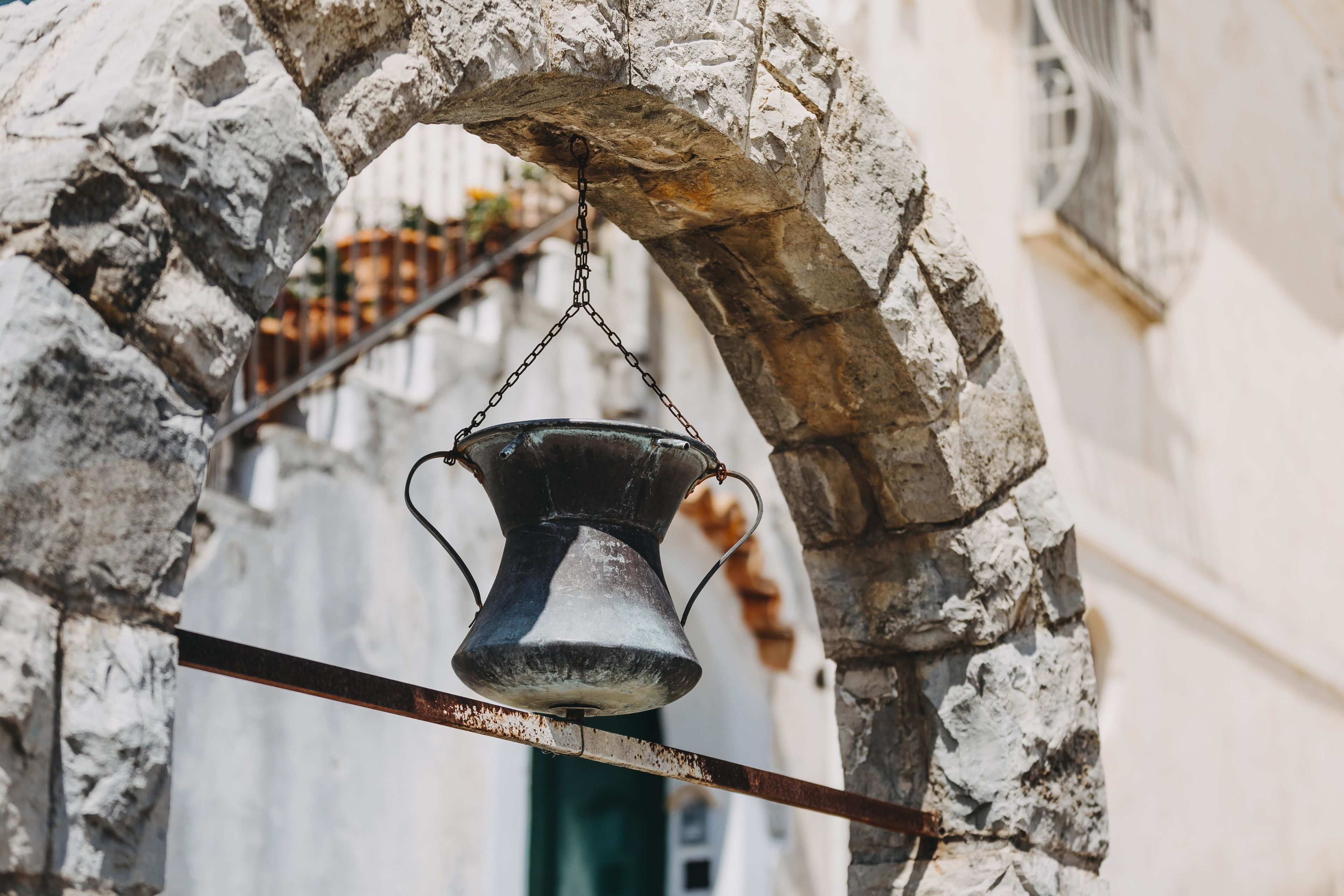 A rustic stone archway with a metal bell hanging from it.