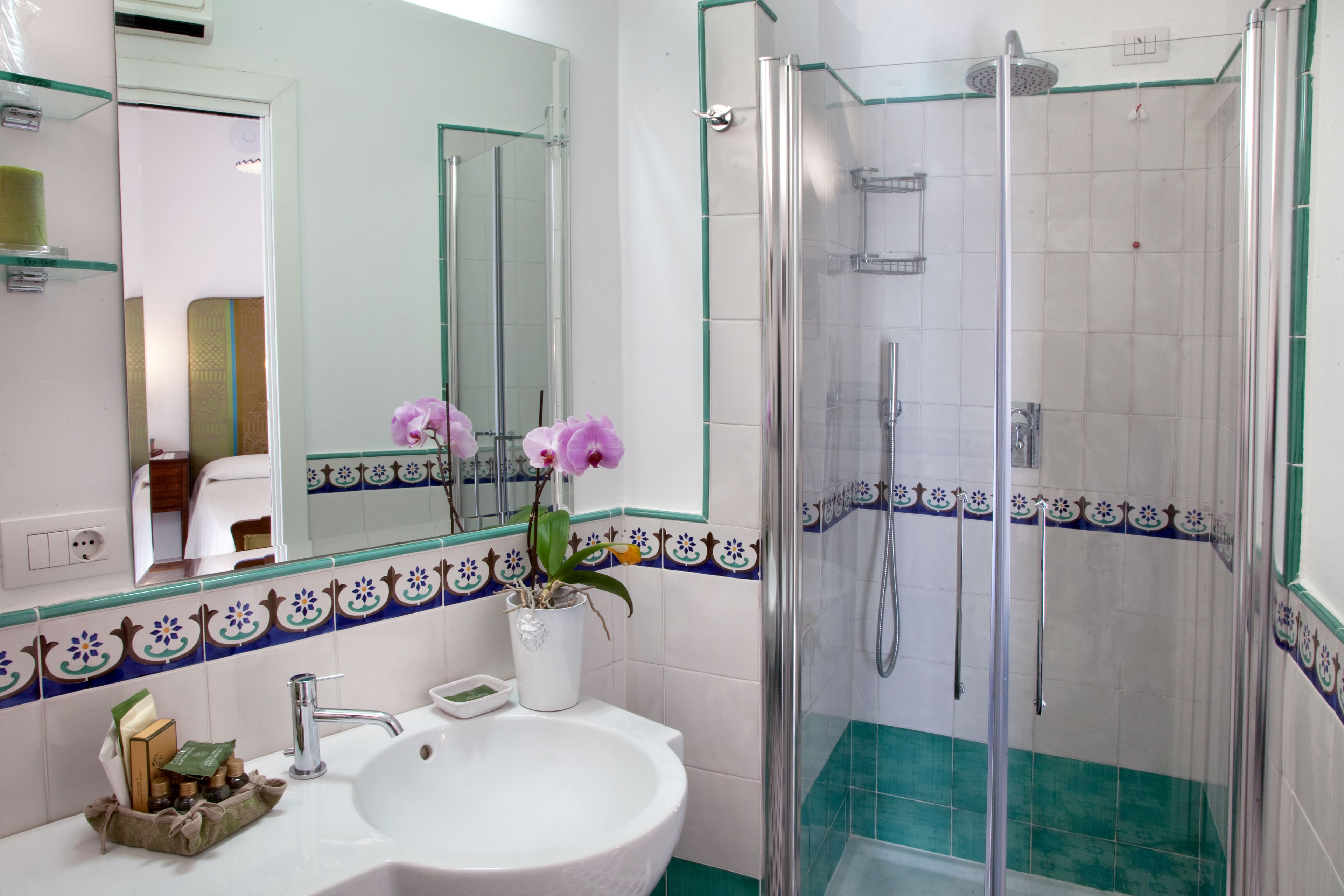 A bathroom with a white sink, a glass shower enclosure, and a mirror with a decorative tile border.