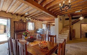 A rustic dining area with a wooden table set for four, surrounded by stone walls and a vaulted ceiling. - Kirithra (Neo Chorio)