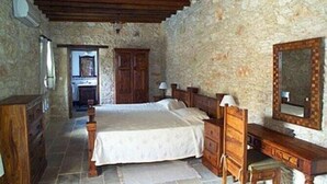 A bedroom with a stone wall, wooden bed, dresser, and a mirror. - Kipseli (Neo Chorio)