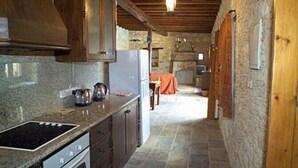 A rustic kitchen with a stone floor, wooden cabinets, and a built-in oven. - Kipseli (Neo Chorio)