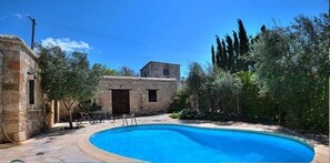 Une piscine entourée de bâtiments en pierre et de verdure.
