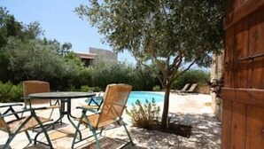 An outdoor patio with a pool, surrounded by greenery and a wooden gate. - Kipseli (Neo Chorio)