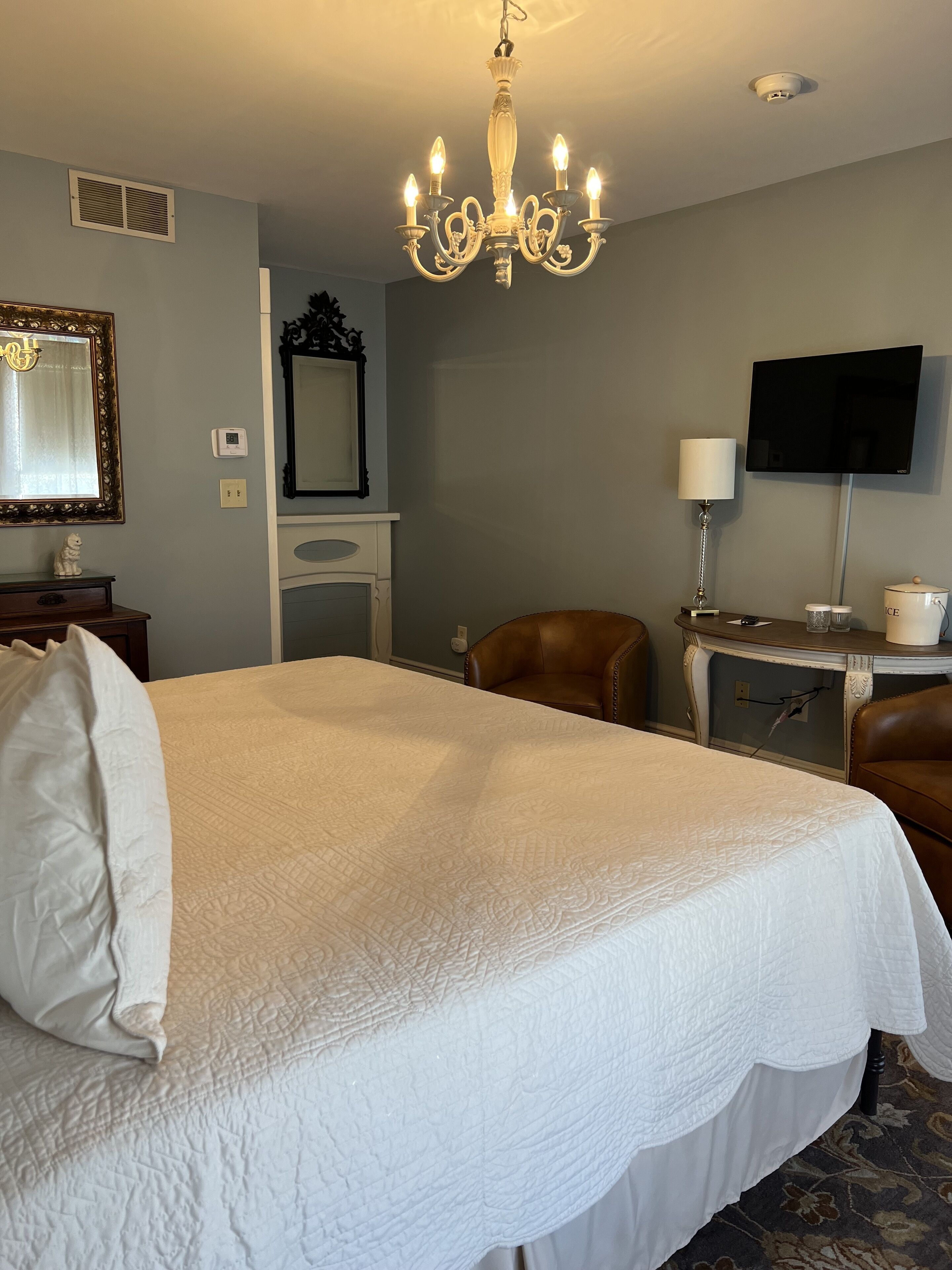 A hotel room with a large bed, a chandelier, a television, a desk, and a chair.