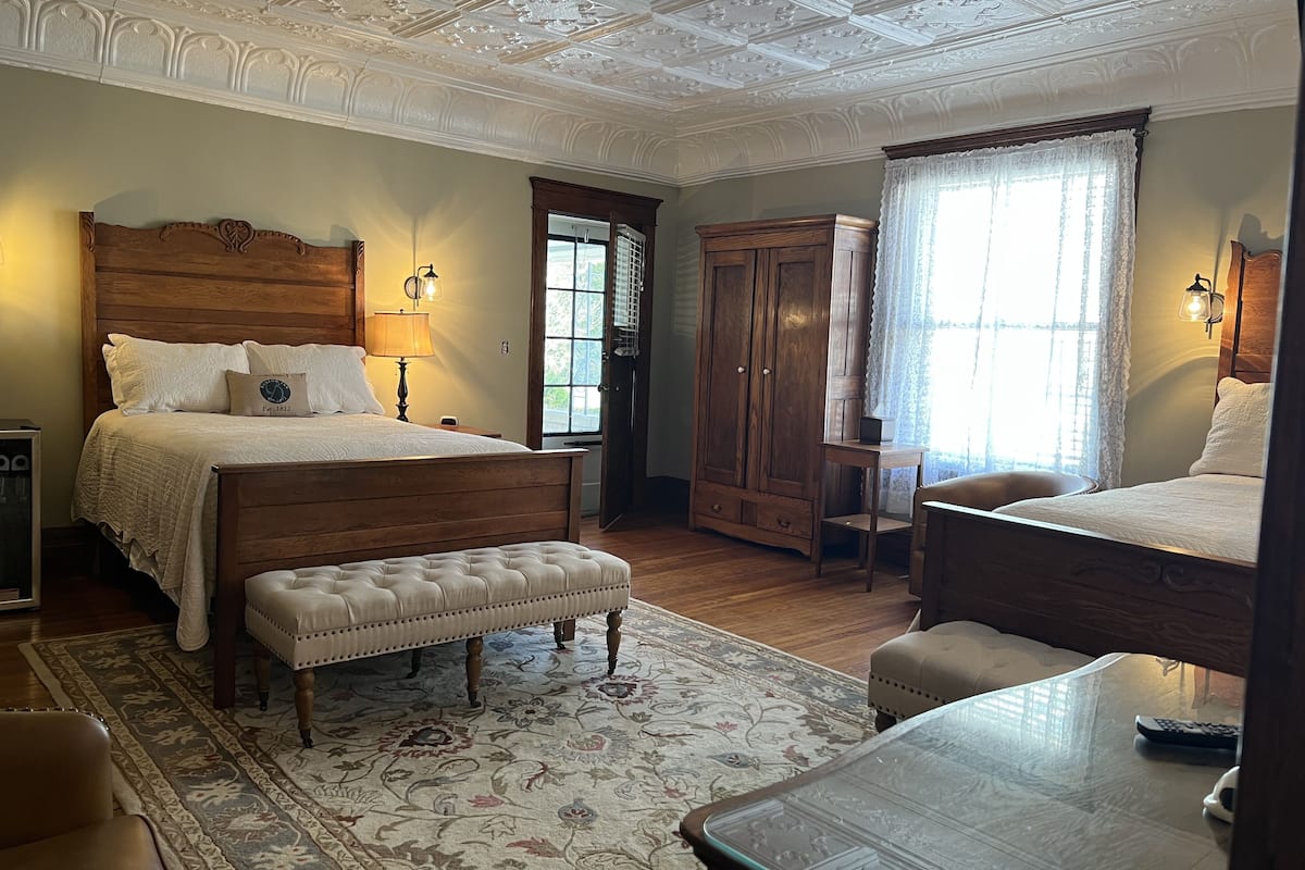 Une chambre à coucher avec un grand lit, une armoire en bois, un bureau et une fenêtre avec des rideaux.