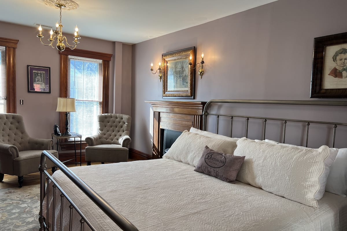 Une chambre à coucher avec un grand lit, deux fauteuils, un lustre et une cheminée.