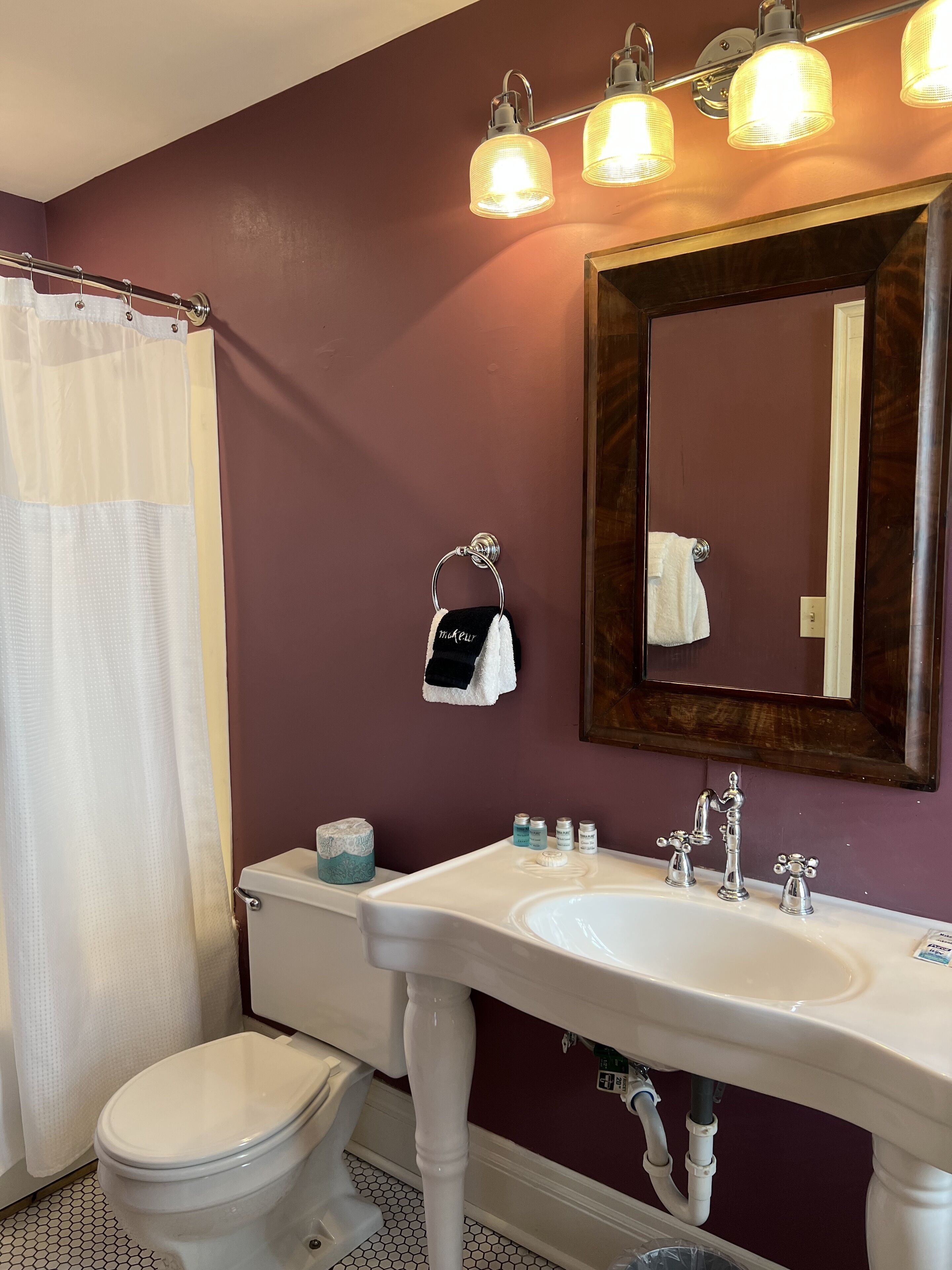 Un baño con inodoro blanco, lavamanos blanco con espejo encima y cortina de ducha.