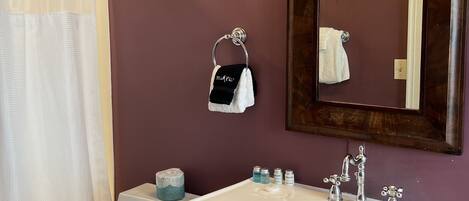 Un baño con inodoro blanco, lavamanos blanco con espejo encima y cortina de ducha.