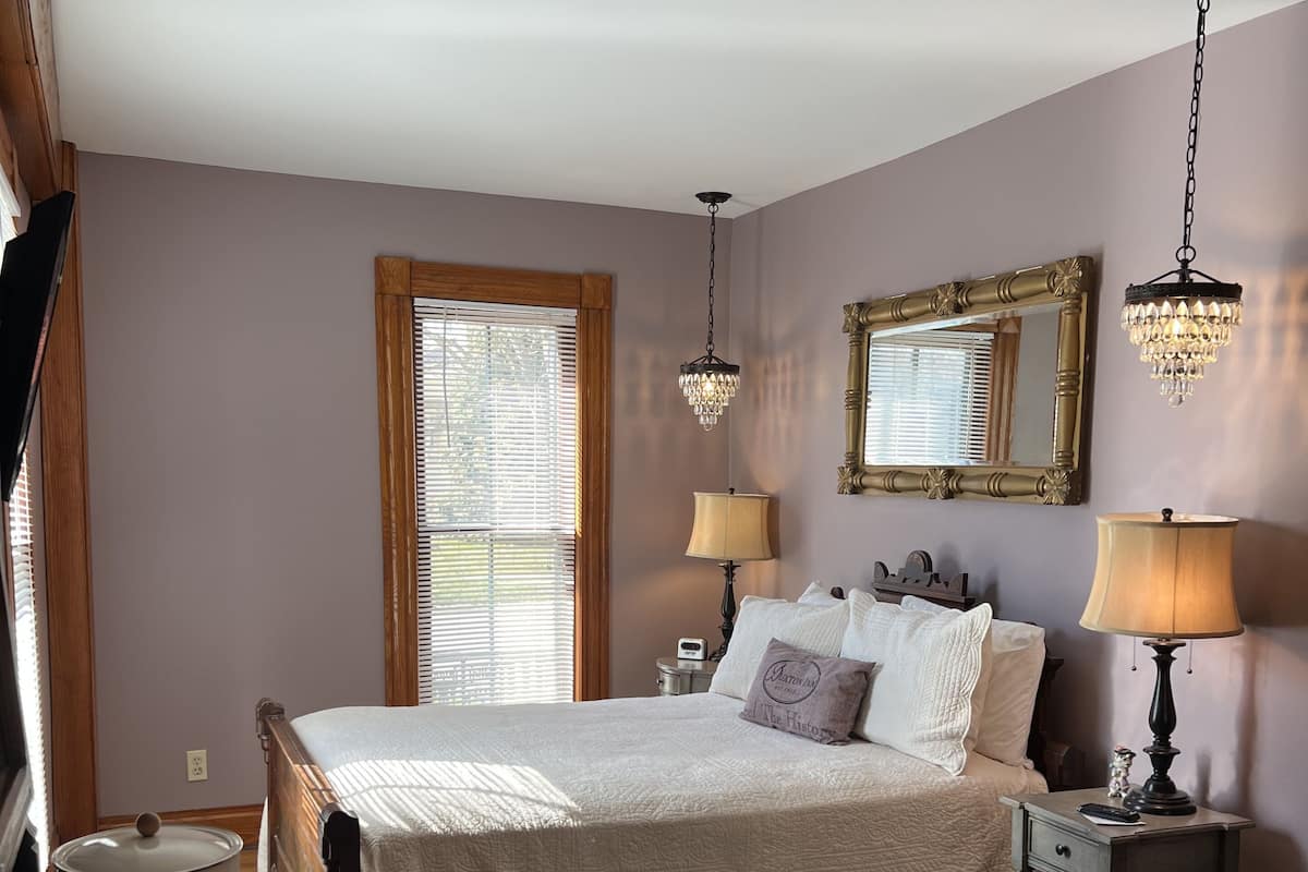 Une chambre à coucher avec un lit, des lampes de chevet, une table de chevet, un miroir et une fenêtre avec des stores.