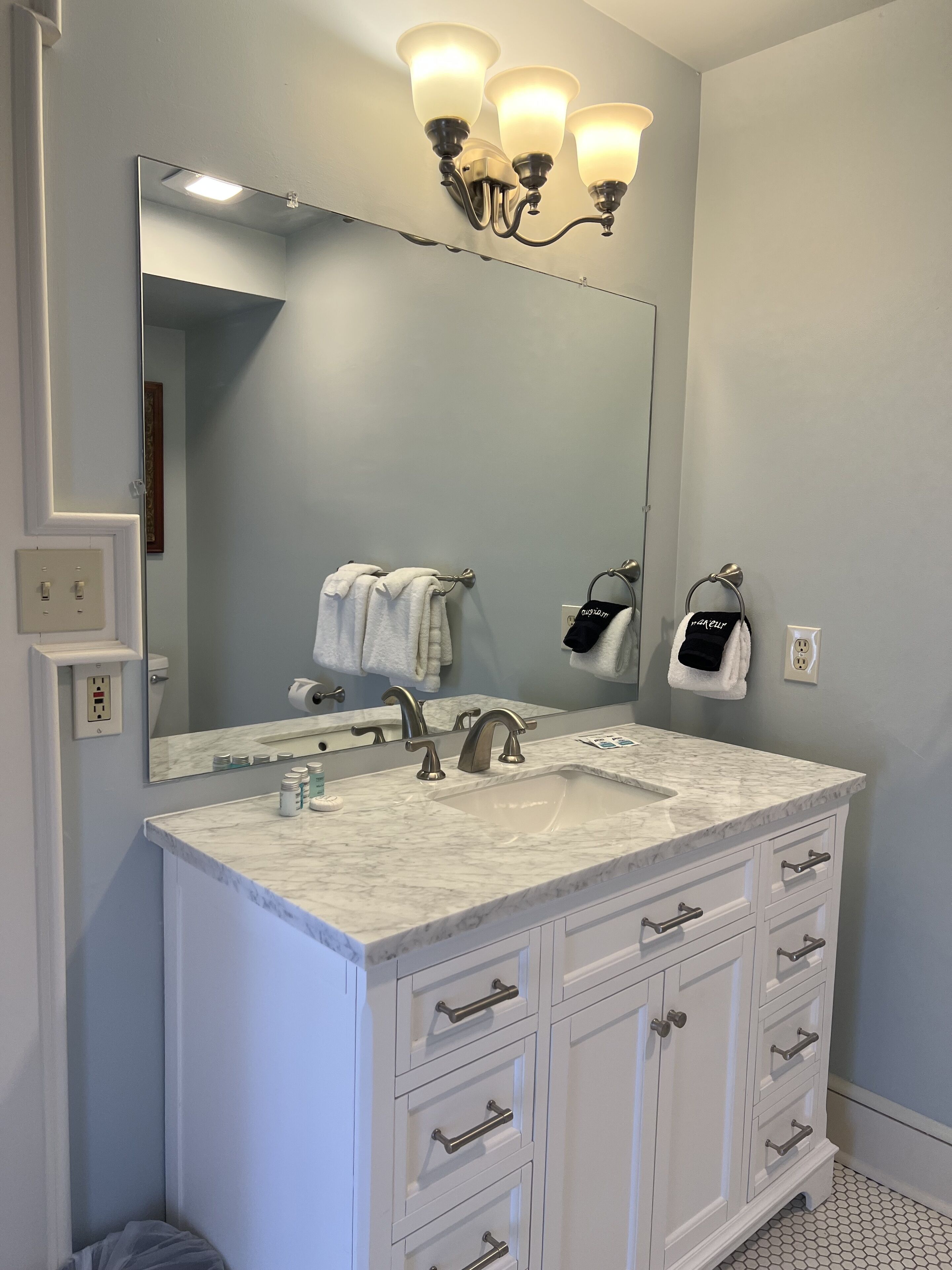 A bathroom with a large mirror, a sink with a marble countertop, and a vanity with drawers.