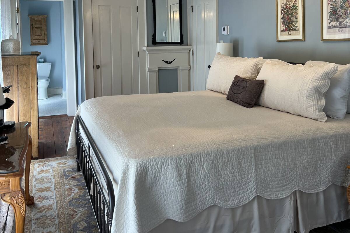 Une chambre à coucher avec un grand lit, un lustre, une commode, un miroir et des œuvres d’art encadrées accrochées au mur.