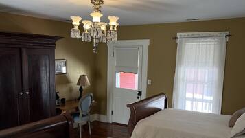 Une chambre avec deux lits, une armoire en bois, un bureau avec une chaise, un lustre et une fenêtre avec des rideaux.