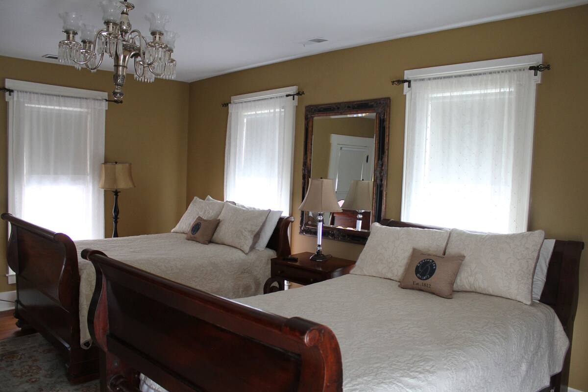 Une chambre d’hôtel avec deux lits en bois, un lustre, un grand miroir et une fenêtre avec des rideaux.