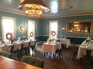 Zona pranzo con tavoli apparecchiati per un pasto, con un lampadario, ghirlande e un quadro appeso al muro.