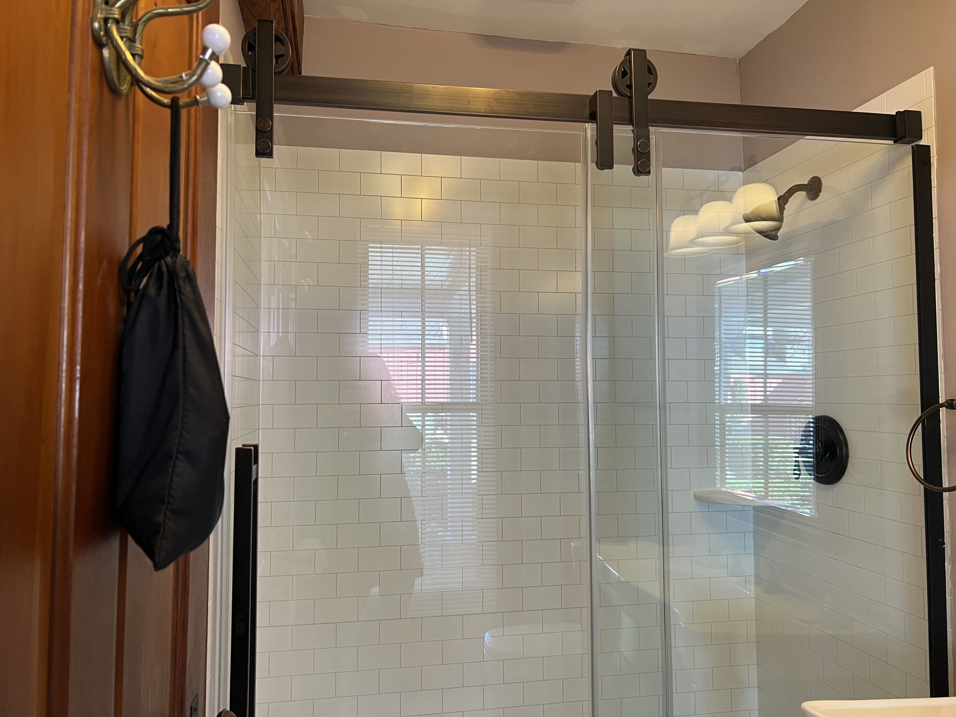 Een moderne badkamer met witte metrotegels, een glazen douchecabine en een houten deur.